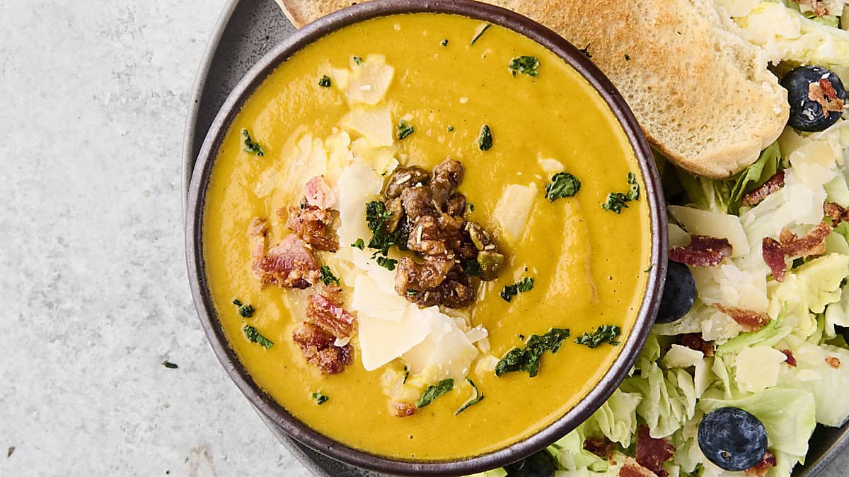 canned pumpkin soup recipe in a bowl with nuts, bacon, and cheese for toppings