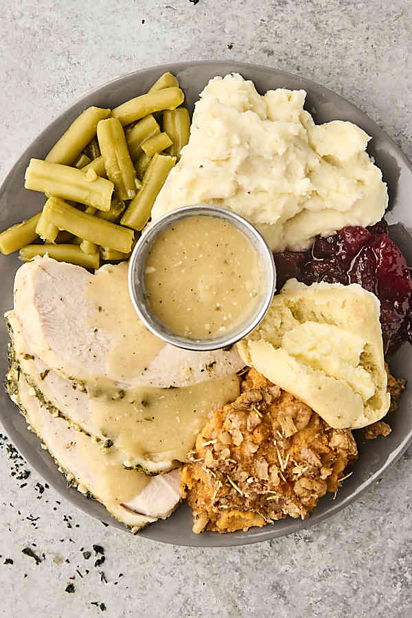thanksgiving dinner on a plate with slow cooker turkey, green beans, mashed potatoes, sweet potato casserole, and more