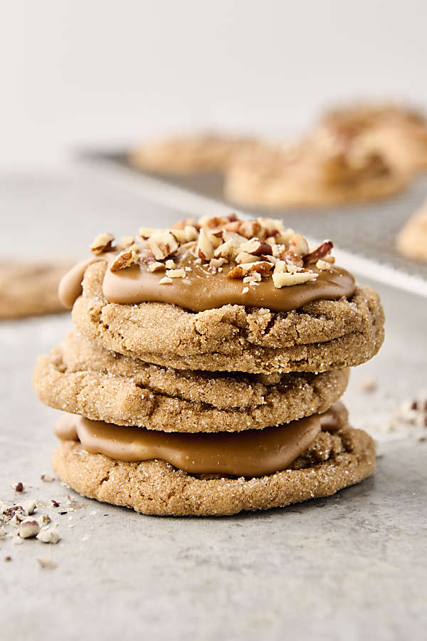 stack of maple brown sugar cookies topped with brown sugar maple frosting and chopped peans