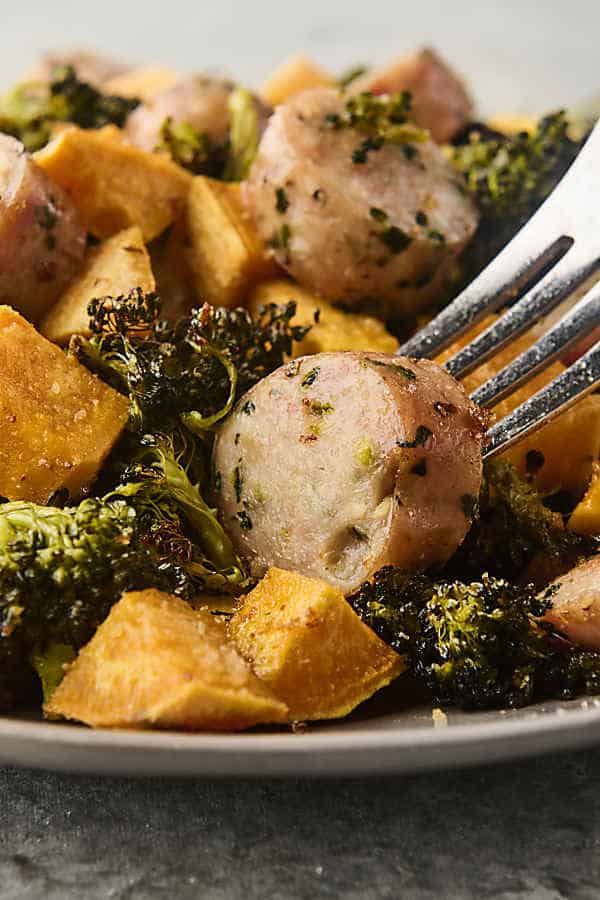 using a fork to scoop up chicken sausage with sweet potato and broccoli