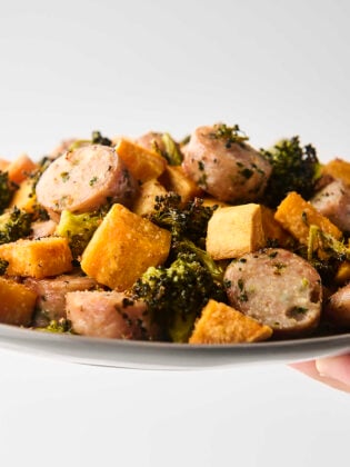 holding a plate of roasted chicken sausage with vegetables