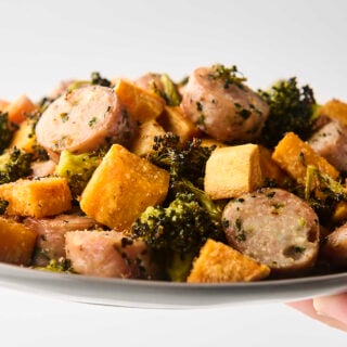 holding a plate of roasted chicken sausage with vegetables