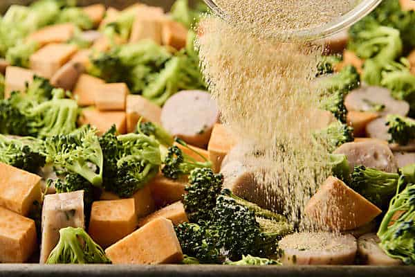 sprinkling chicken sausage, broccoli, and sweet potato with spices