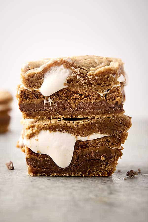 stacking two cookie butter smores bars on top of each other with marshmallow fluff oozing out