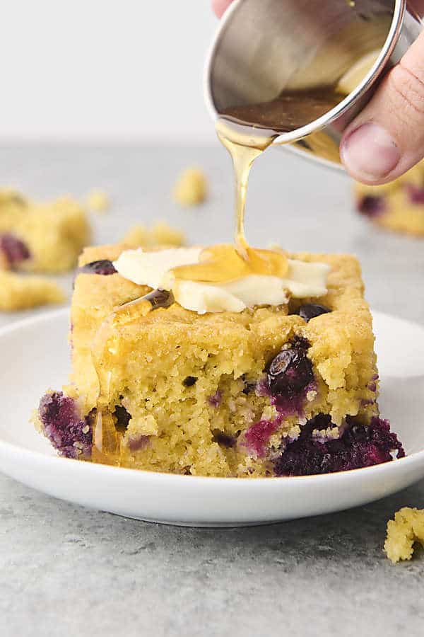 drizzling honey on a piece of blueberry cornbread