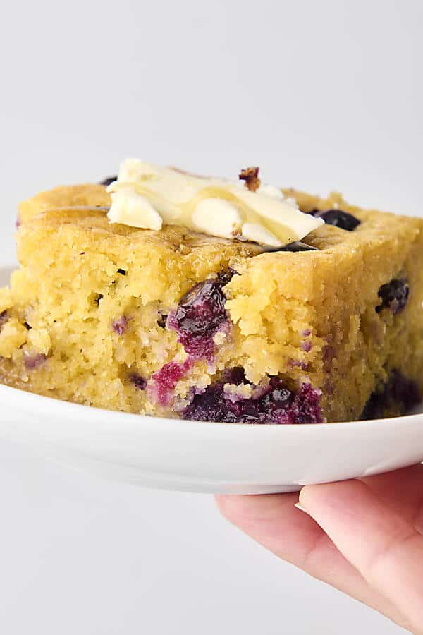 holding a piece of blueberry cornbread topped with butter