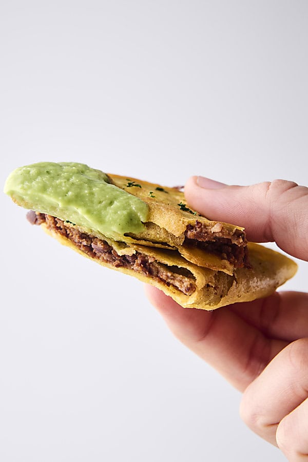 vegan black bean taco dunked in avocado sauce