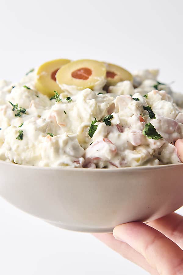 holding a bowl of dirty martini dip topped with olives