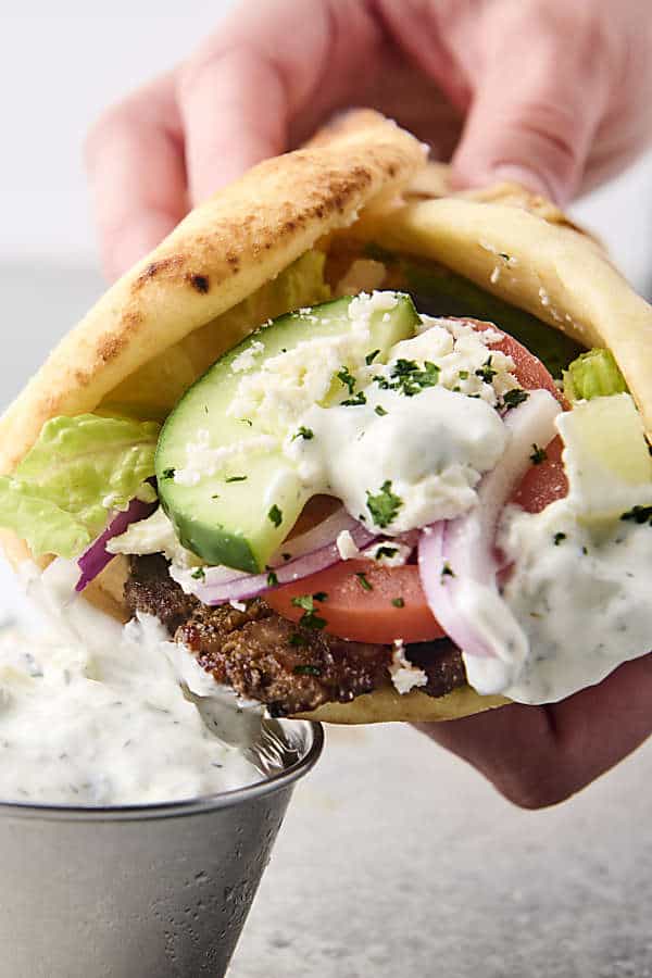 holding a beef and pork gryo with tzatziki, lettuce, tomatoes, onion, and feta