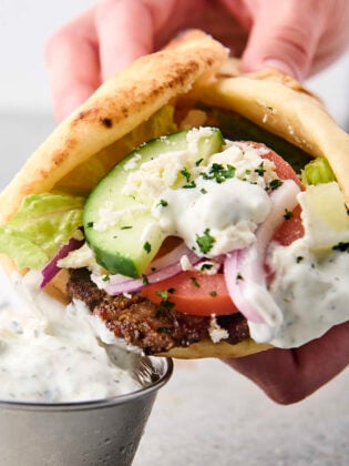 holding a gryo with tzatziki, lettuce, tomatoes, onion, and feta