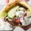 holding a gryo with tzatziki, lettuce, tomatoes, onion, and feta