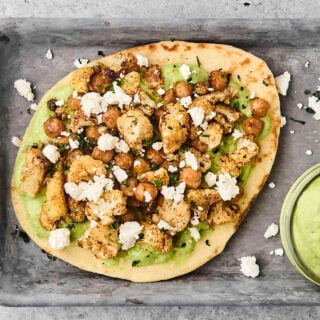 roasted cauliflower and chickpea pita on a tray with avocado sauce
