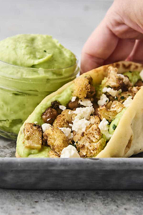 holding a roasted cauliflower and chickpea pita topped with feta
