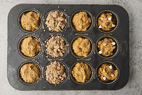pumpkin muffins in a muffin tin showing various toppings and mix-ins