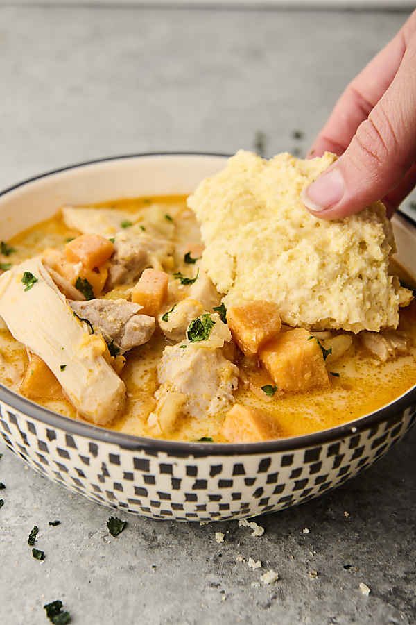dunking a biscuit into a bowl of chicken stew
